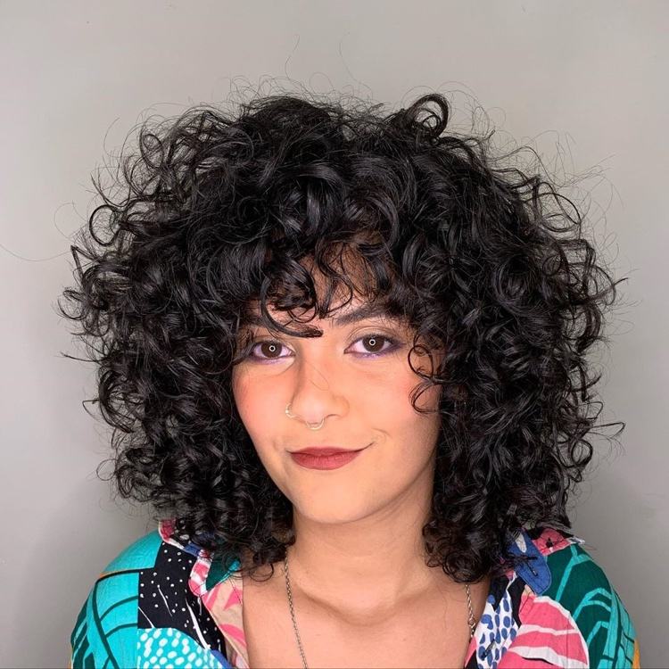 Părul creț lung până la umeri, cu breton și mult volum pe vârful capului