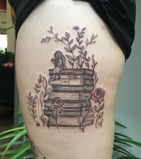 花、葉、それに座っている女の子と本のスタック太もものタトゥー。