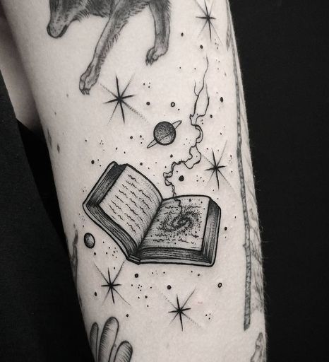 Livre ouvert avec tatouage étoiles, planète et cyclone.