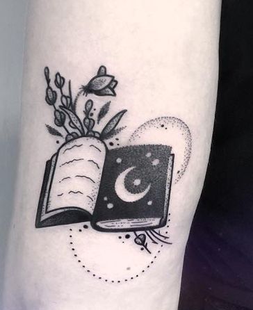 Livre ouvert avec tatouage croissant de lune, étoiles, fleurs et feuilles.