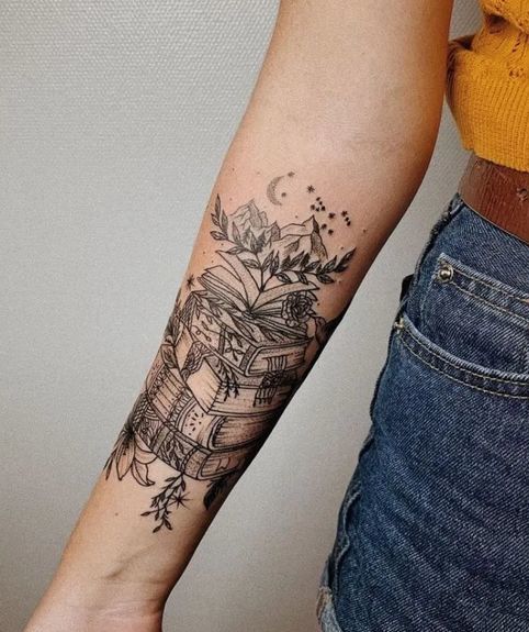 Livre avec tatouage croissant de lune, fleurs et feuilles sur l'avant-bras ou une femme
