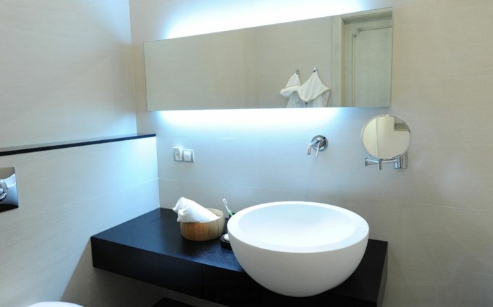 Iluminatul indirect este creat aici de lămpile din spatele oglinzii din baie iluminare oglindă spate rotundă lavoar consolă neagră