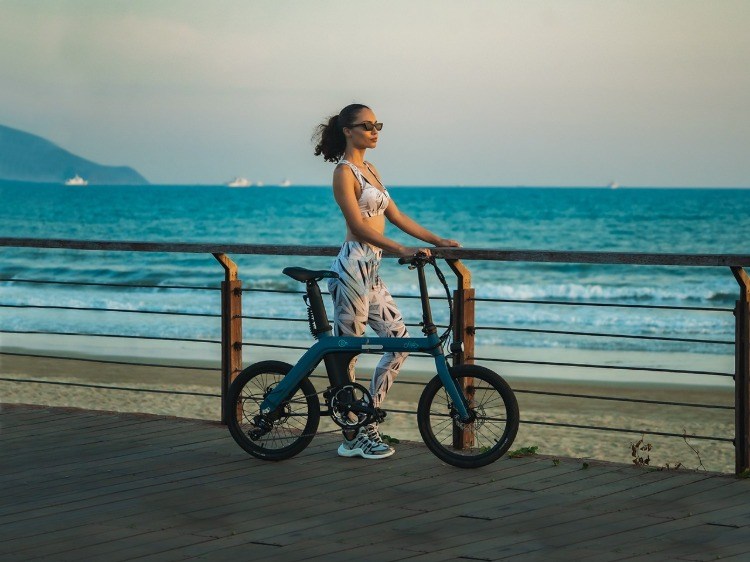 femeia cu bicicleta electrică pliabilă se bucură de apusul soarelui pe plajă