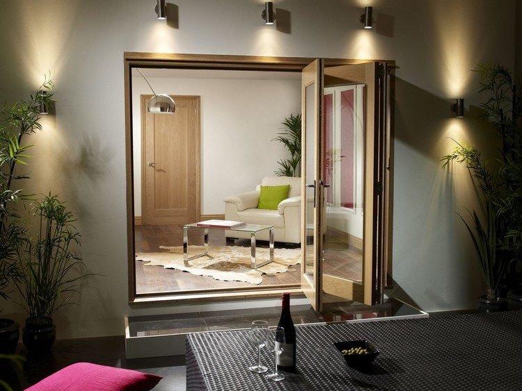 Uși de sticlă pliante deschise pentru terasă cu iluminare usi de sticla pliante-terasa-lemn-scari-iluminat-seara-ratan-masa-roz-perne