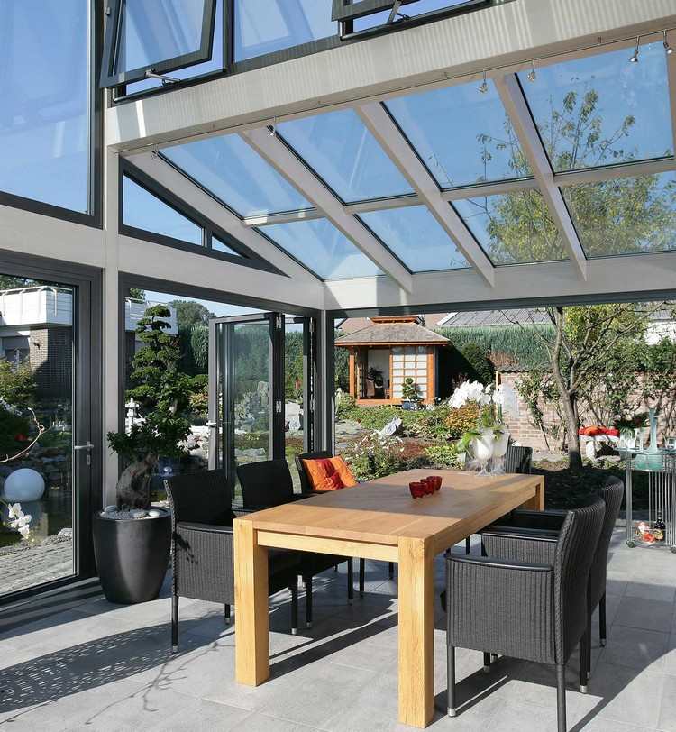 Grădină de iarnă vitrată cu scaune din ratan și o masă din lemn pliante-sticla-usi-gradina de iarna-lumina soarelui-completa-geam-scaune din ratan-masa din lemn