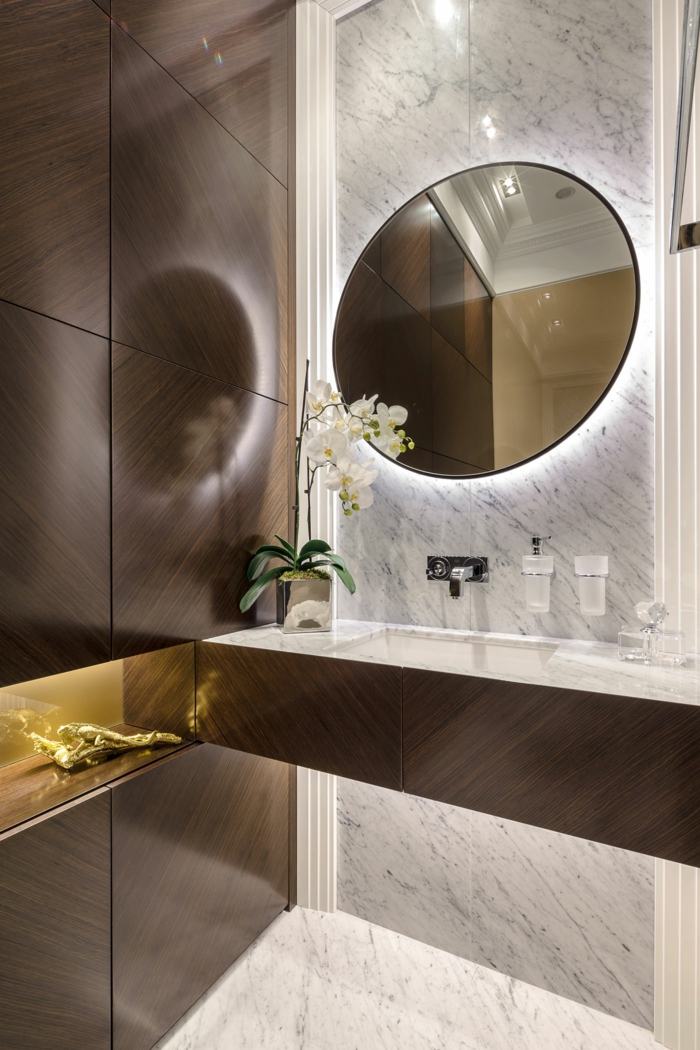 Baia mică de lux din apartament cu oglindă rotundă dulap baie baie maro închis lemn marmură albă consolă orhidee
