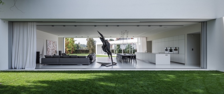 cameră de zi albă și gri zonă de zi statuie zonă de luat masa bucătărie neagră uși glisante fără mână grădină deschisă